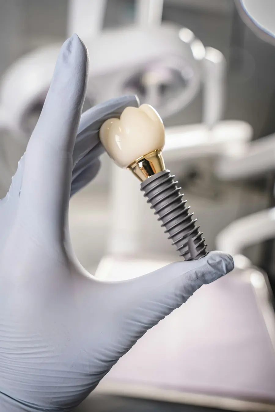 Gloved hand holding a dental implant with a porcelain crown