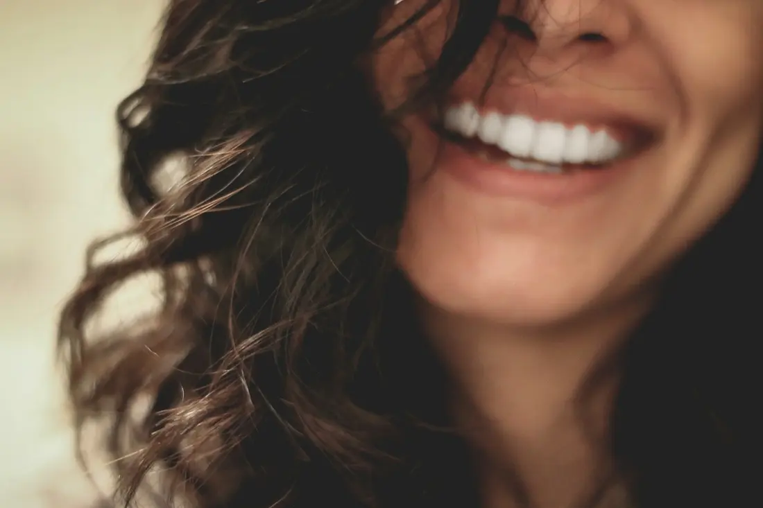 Woman with dark wavy hair laughing with a bright white smile